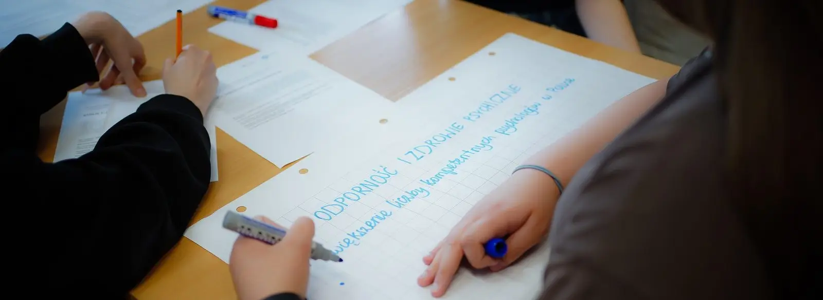Zbliżenie na dłonie uczestniczek zapisujących postulaty na arkuszu
